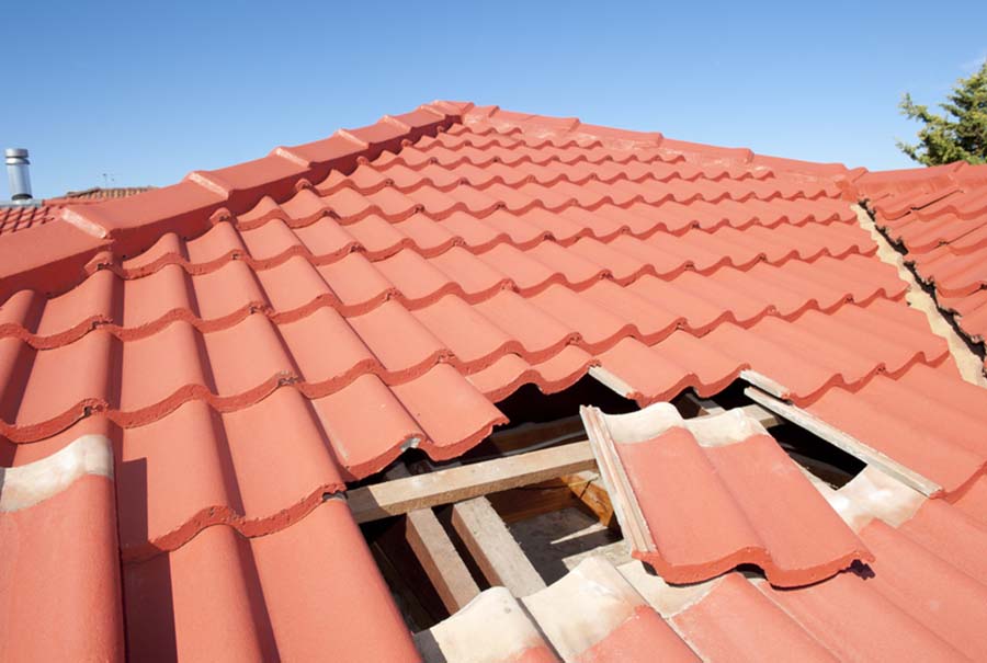 Damaged red tile roof construction house. Damaged roof construction on house needs tiles or shingles repaired and replaced, red tiles and blue sky as background and copy space.