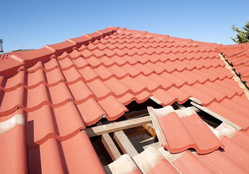 Damaged red tile roof construction house. Damaged roof construction on house needs tiles or shingles repaired and replaced, red tiles and blue sky as background and copy space.